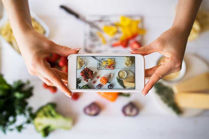 Food blogger tager foto af mad med mobiltelefon.
