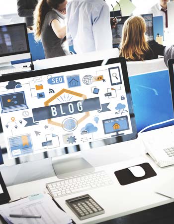 Stemningsbillede til artiklen "Hvad er en blog". Ordet "blog" kan ses på en monitor i forgrunden. I baggrunden ses et travlt kontor.